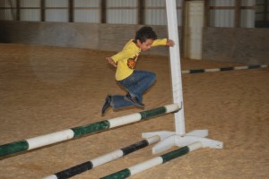 Salman jumps while playing games in the shady indoor arena after his riding lesson - Clairvaux Summer Horse Camp